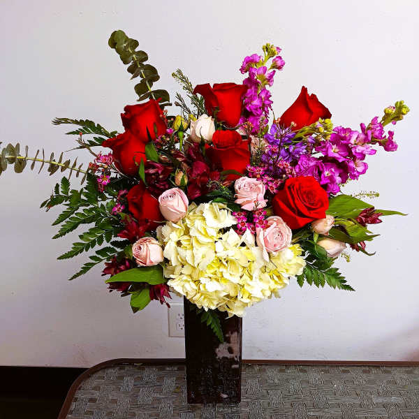 Large bouquet of red and pink roses with pale hydrangeas in a tall vase