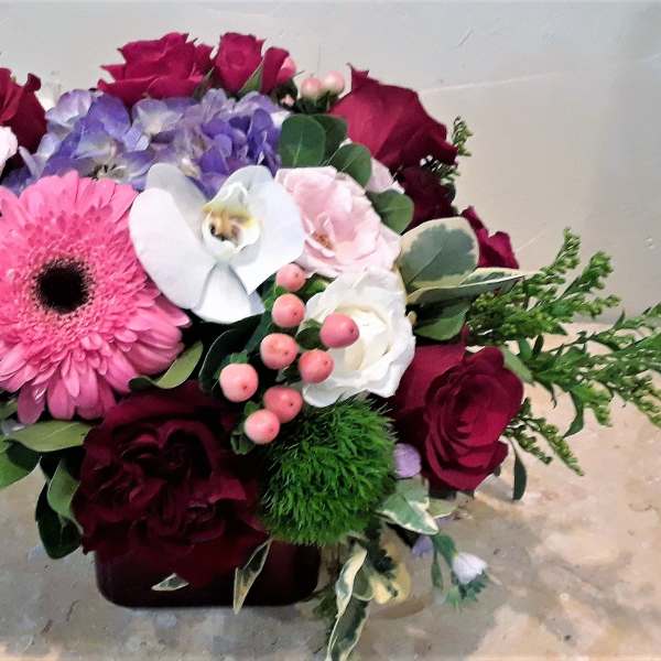 Mixed bouquet with roses, gerbera daisy, orchid, and hydrangea in a low container