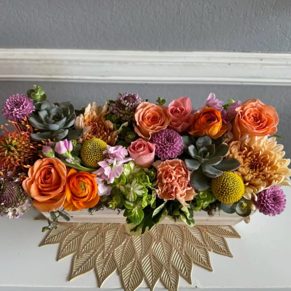 Low rectangular arrangement of orange and pink flowers with succulents