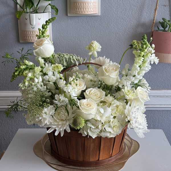 White floral arrangement in a wooden basket with roses and daisies