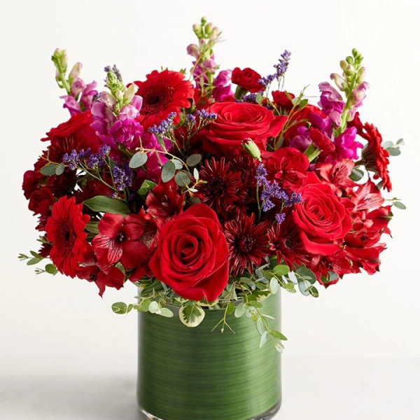 Red roses and mixed red flowers in a green glass vase