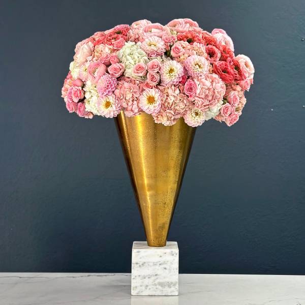 Pink floral arrangement in a gold cone vase on a marble base
