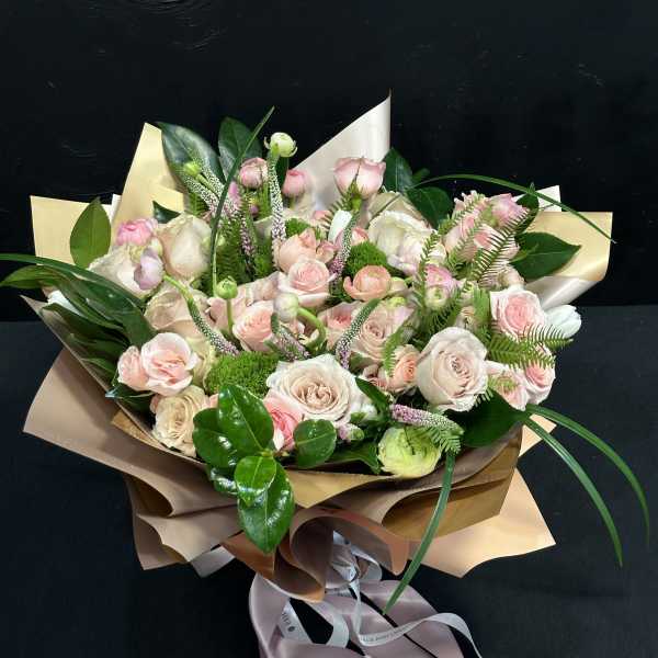 Bouquet of pale pink and white roses wrapped in tan paper