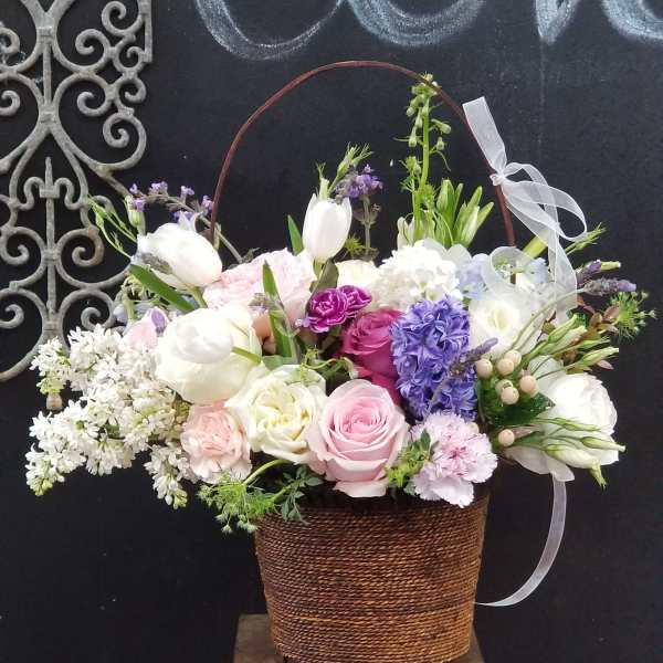 Basket arrangement of pink, white, and purple flowers with a ribbon bow