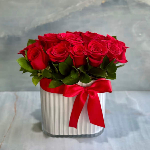 Red roses arranged in a white ribbed box with a red ribbon