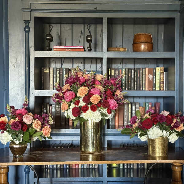Three floral arrangements in gold vases on a table