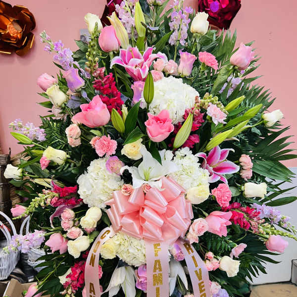 Tall standing spray of pink and white roses, lilies, and carnations with a large pink bow.