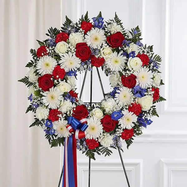 Patriotic standing wreath with red roses, white blooms, and blue flowers on an easel.