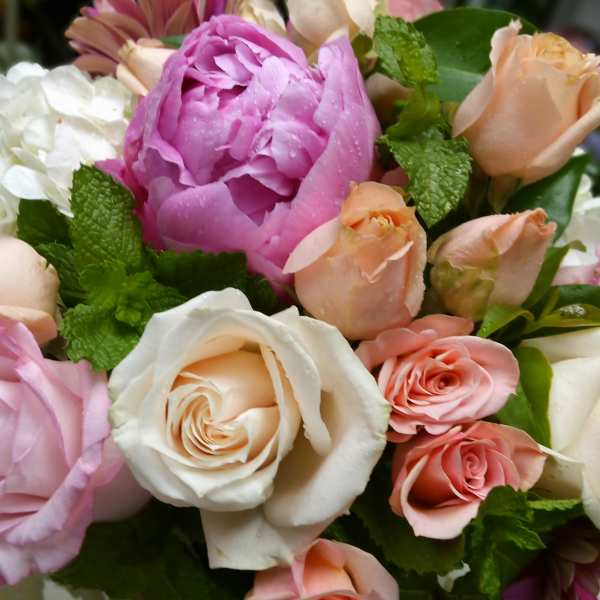 Mixed bouquet of pink, peach, and white roses with a large pink peony