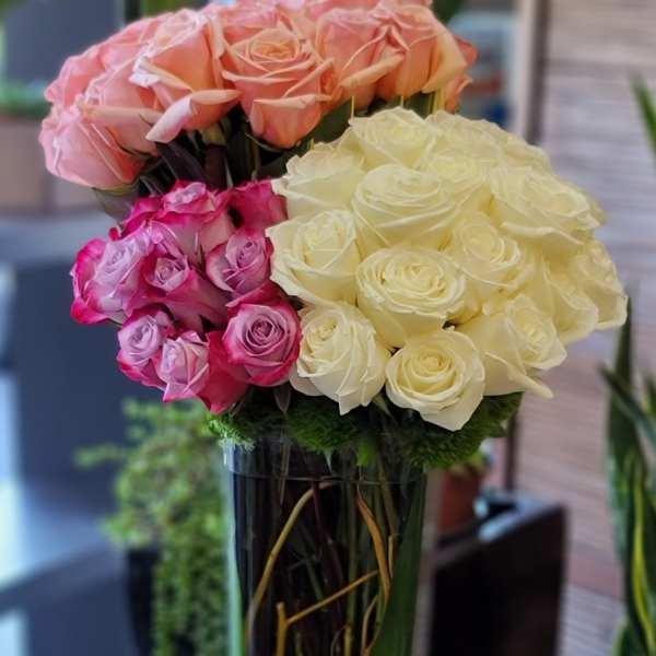 Three clusters of roses in a tall clear vase.