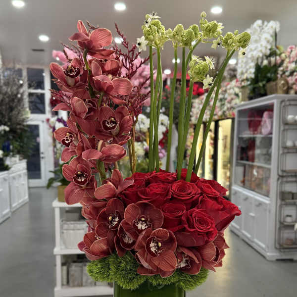 Red roses and orchids arranged in a tall green vase