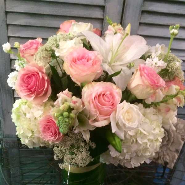 Round arrangement of pink roses, white lilies and white hydrangeas in a clear glass vase