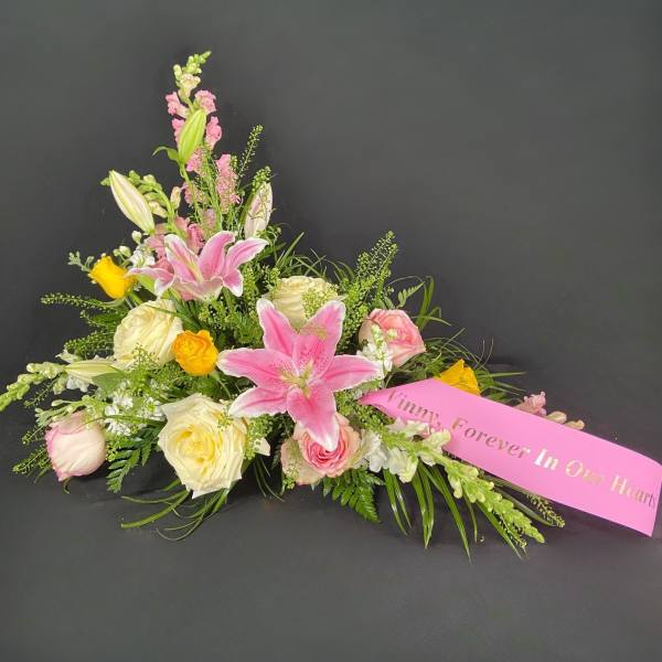 Pink lilies and roses arranged with a memorial ribbon