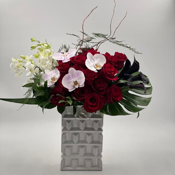 Red roses and white orchids in a tall geometric vase