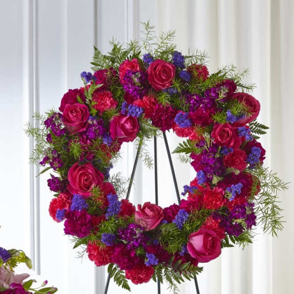 Heart-shaped floral wreath with pink roses and purple flowers on a stand