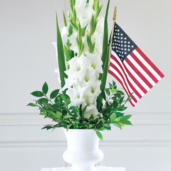 White gladiolus arrangement in a white urn with an American flag