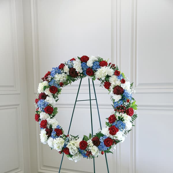 Circular floral wreath on a metal stand with red, white, and blue flowers