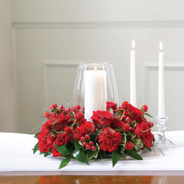 Red floral centerpiece with three white candles in glass holders