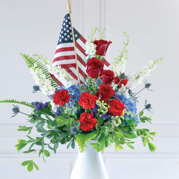 Red roses and blue-white flowers in a white vase with small American flags