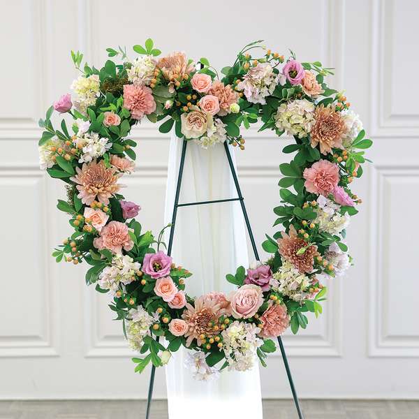 Heart-shaped floral wreath on a stand with pink and white flowers