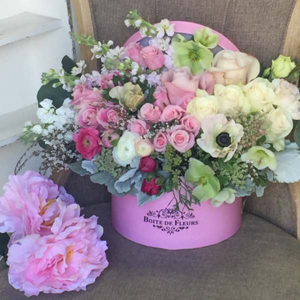 Pink and cream roses arranged in a pink hat box with pastel blooms