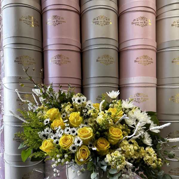 Yellow roses and white daisies arranged in a round hat box