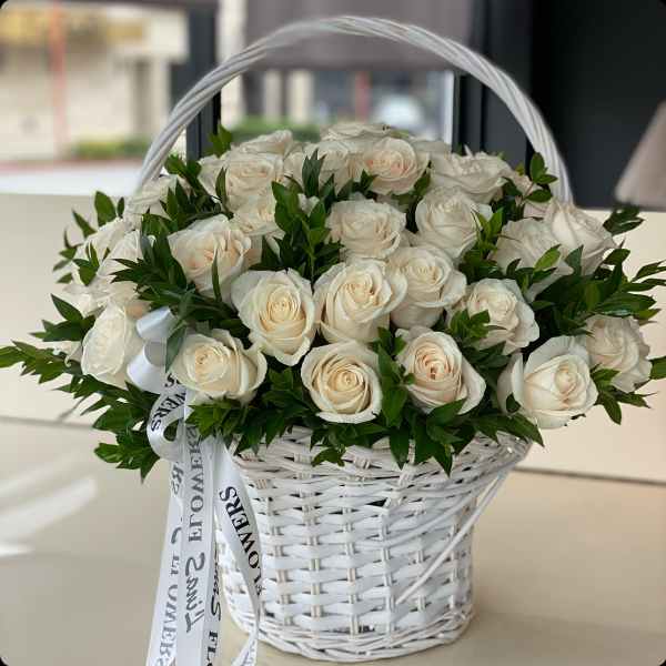 White roses arranged in a white wicker basket with a ribbon