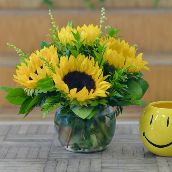 Yellow sunflowers in a clear glass vase beside a yellow smiley mug