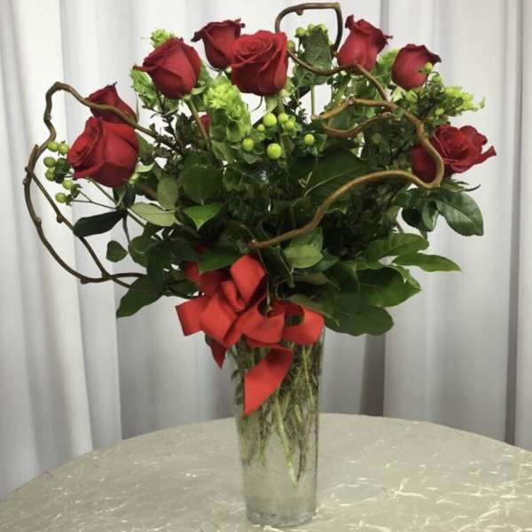 Red roses in a tall glass vase with a red ribbon
