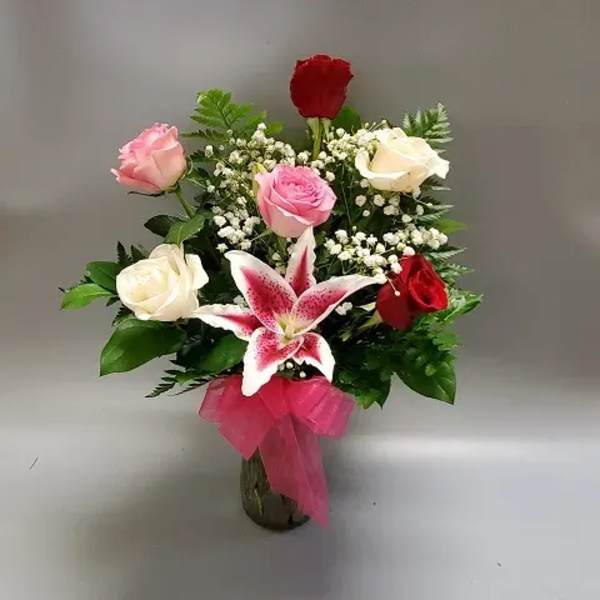 Bouquet of pink, white, and red roses with a pink lily in a vase