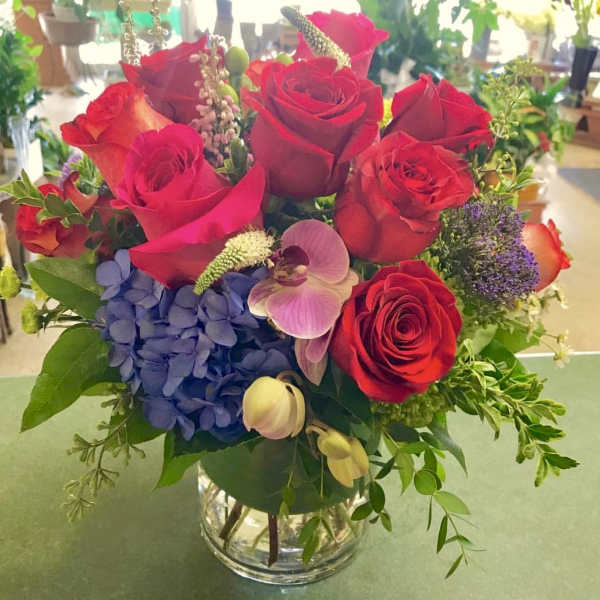 Red roses with blue hydrangea and orchids in a glass vase