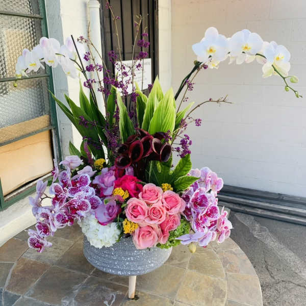 Large floral arrangement with pink roses, orchids, and white orchids in a gray vase