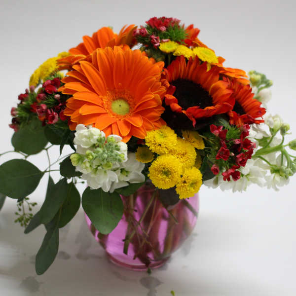 Bouquet of orange gerbera daisies and yellow flowers in a pink glass vase