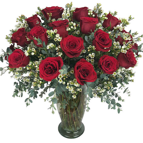 Red roses arranged in a clear glass vase with small white filler flowers