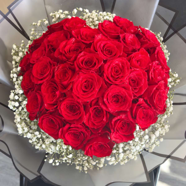 Round bouquet of red roses with white baby's breath in gray wrap
