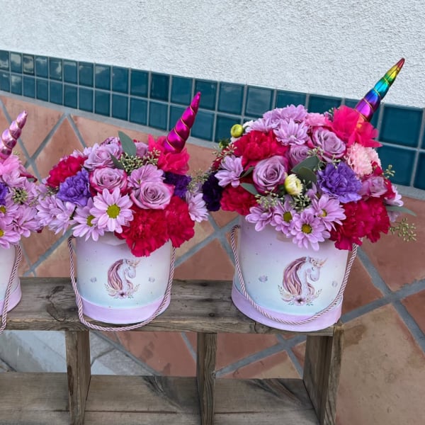 Three unicorn-themed flower buckets filled with pink and purple blooms