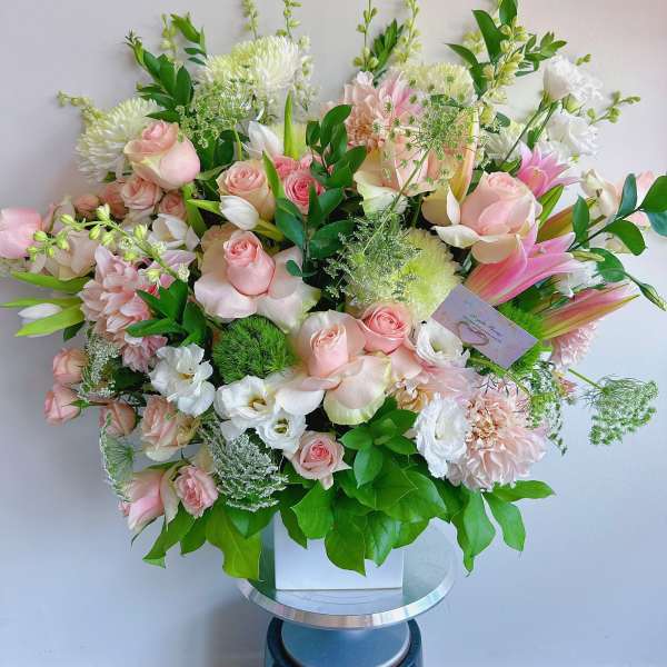 Large pastel bouquet with pink roses, white blooms, and green foliage in a white box