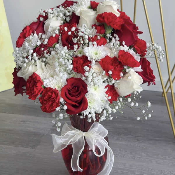 Red and white rose bouquet in a red glass vase with a white ribbon