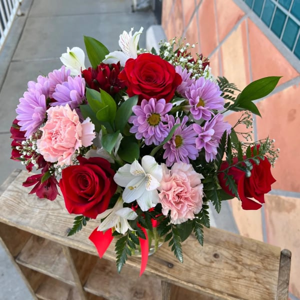 Bouquet of red roses, pink carnations, and purple daisies in a glass vase
