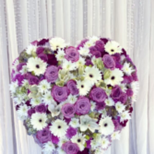 Heart-shaped floral arrangement of purple and white flowers on a stand