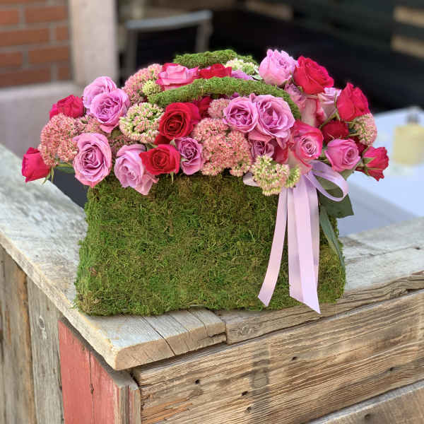 Pink and red roses arranged in a moss-covered box with a ribbon