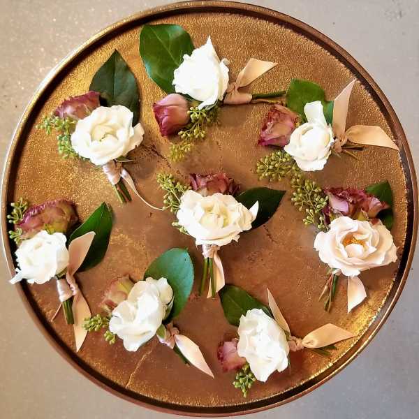Small white rose boutonnieres arranged on a round gold tray