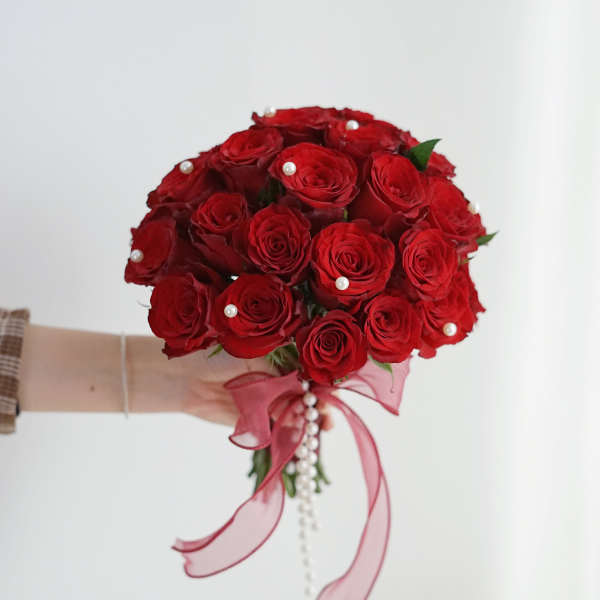 Handheld bouquet of red roses with pink ribbon and pearl accents