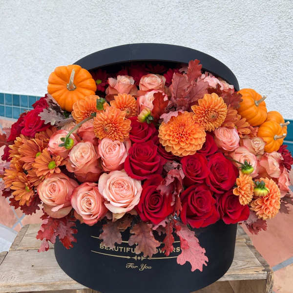 Orange pumpkins and red, peach, and orange flowers in a black hatbox