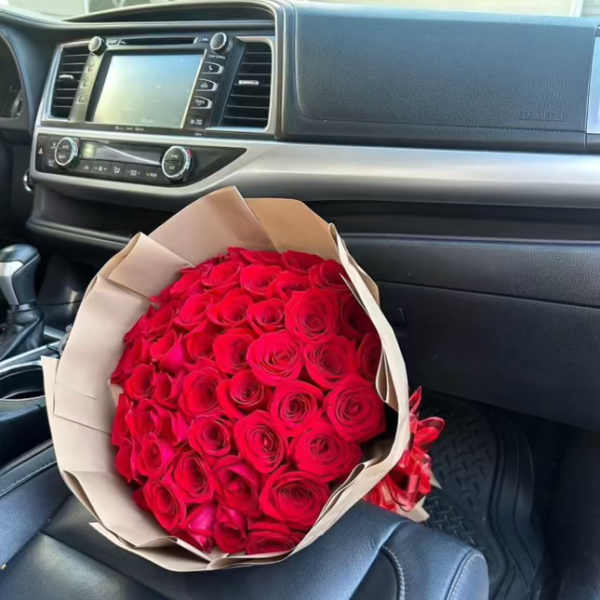 Bouquet of red roses wrapped in beige paper on a car seat