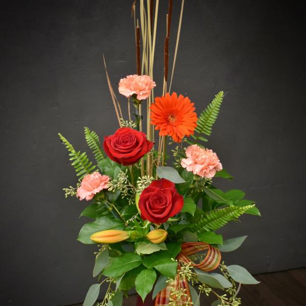 Tall red and peach floral arrangement in a burgundy vase with ribbon