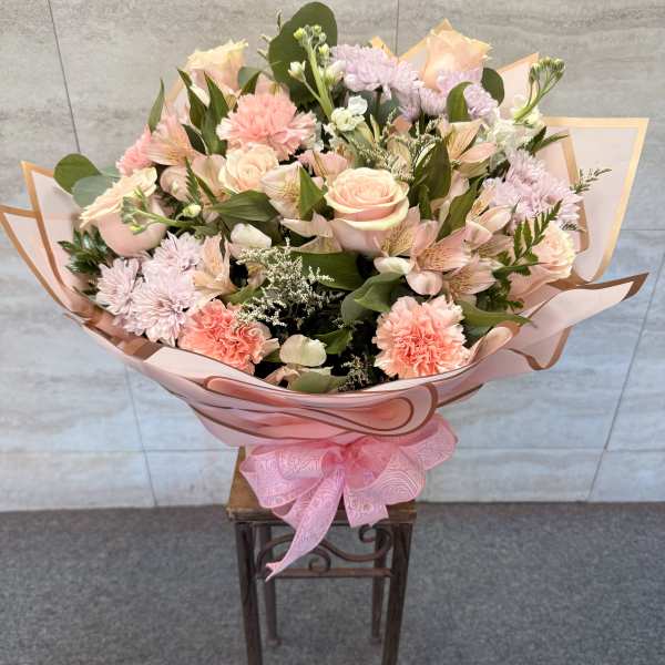 Large bouquet of pink and peach flowers wrapped in pink paper with a ribbon