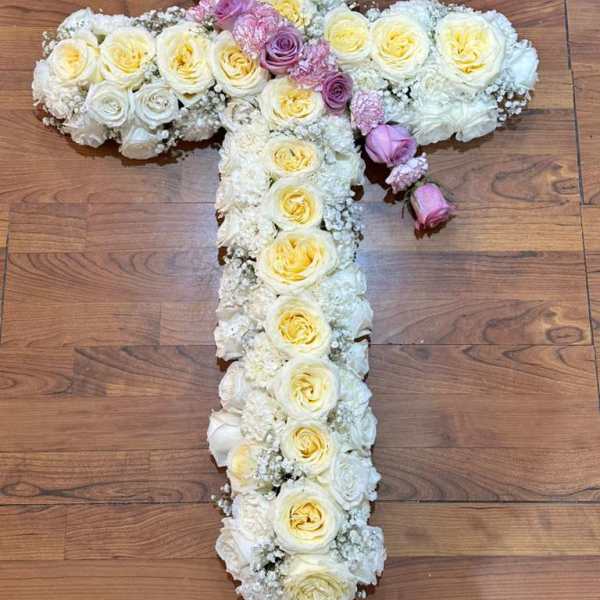 Cross-shaped floral arrangement of white and pale yellow roses with pink accents