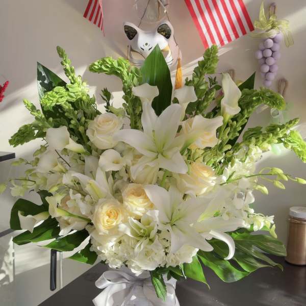 White lilies and cream roses in a white basket with a ribbon