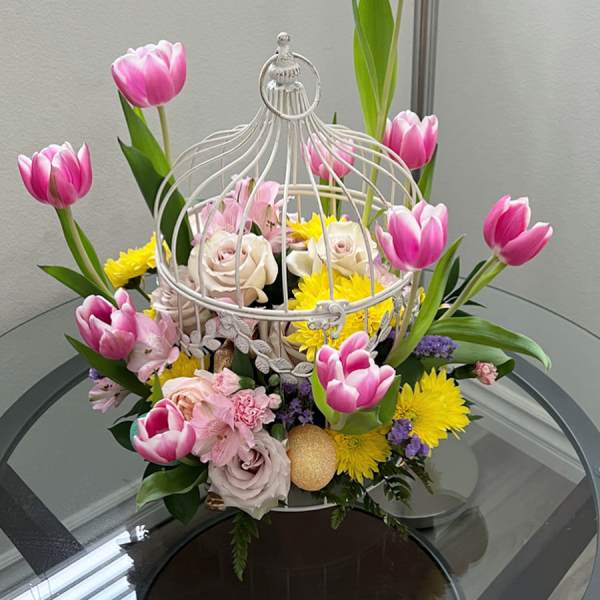Pink tulips and mixed flowers arranged in a white birdcage centerpiece